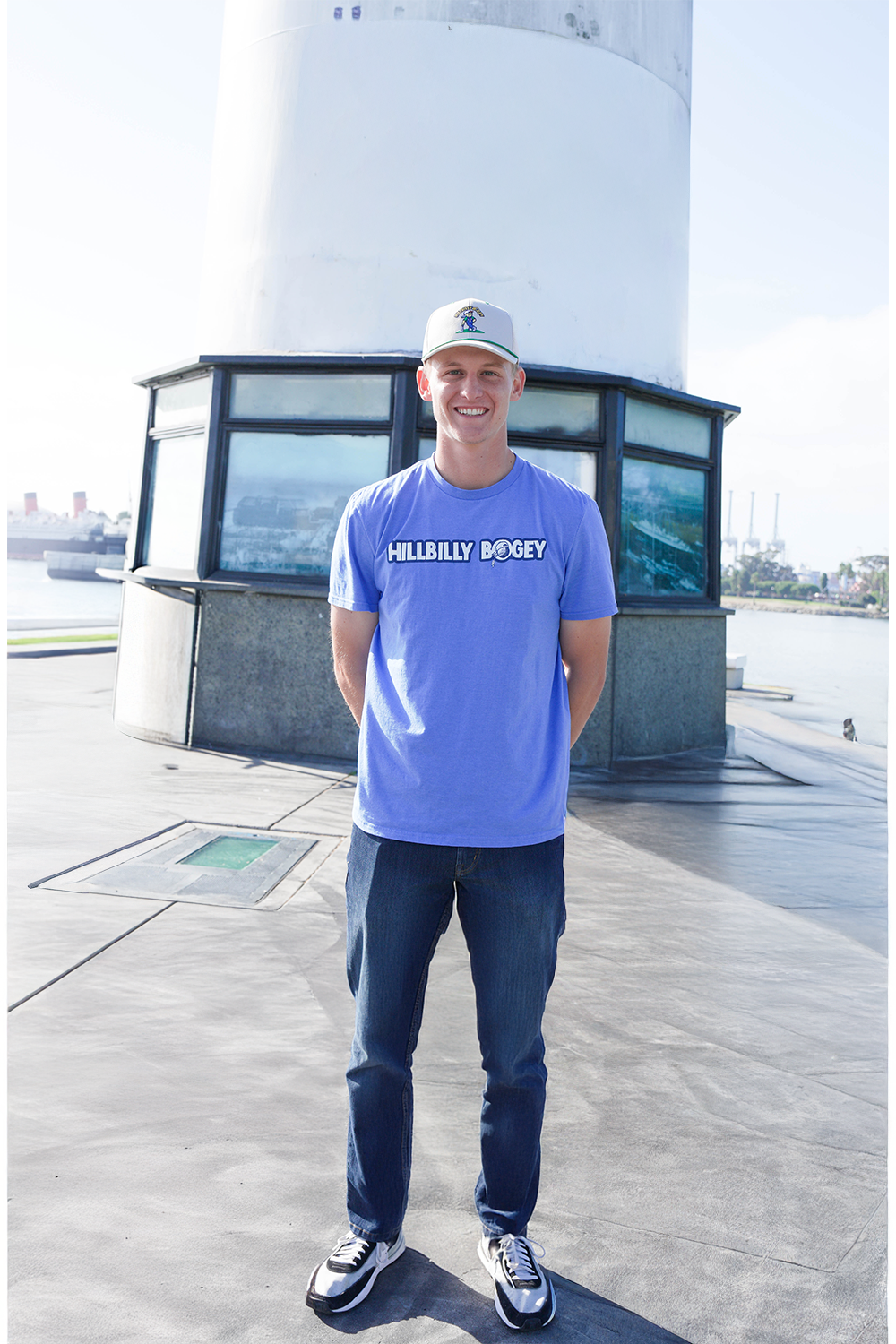 Trent wearing a blue t-shirt with text standing on a dock with a lighthouse in the background